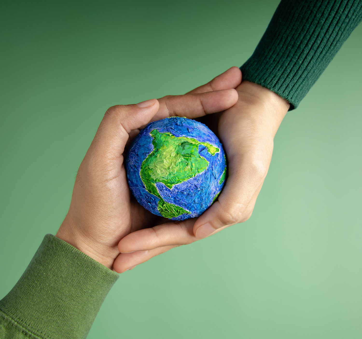 Image showing two different hands cupping a single globe together, symbolizing a collaborative effort in environmental sustainability and planet care.